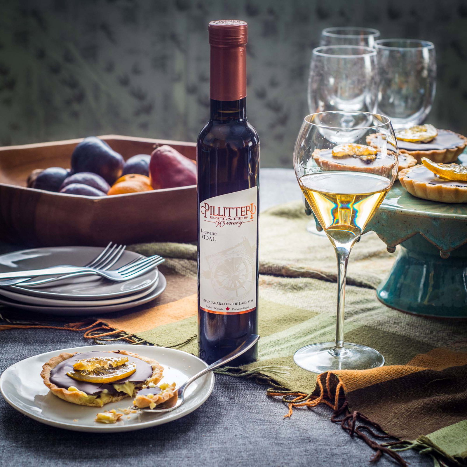 A bottle of Pillitteri Estates Winery Icewine Vidal stands next to a glass of white wine and chocolate tarts.