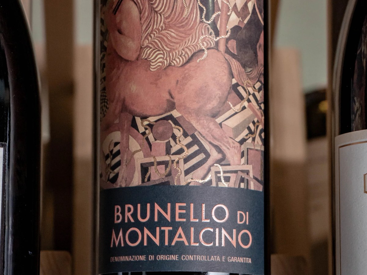 A close-up of a Castello Romitorio Brunello di Montalcino wine bottle, featuring an ornate label with a figure and geometric patterns.