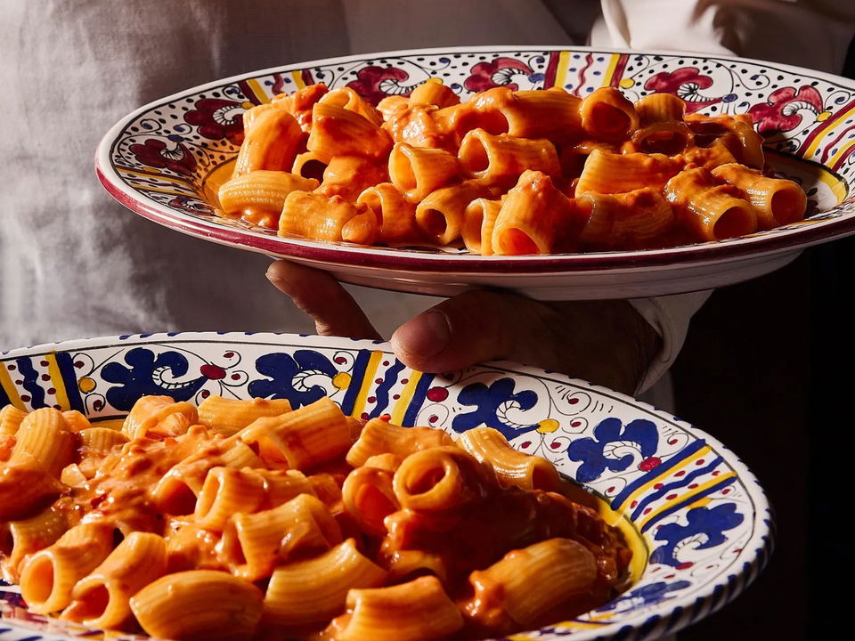 Two plates of pasta with red sauce, held by servers