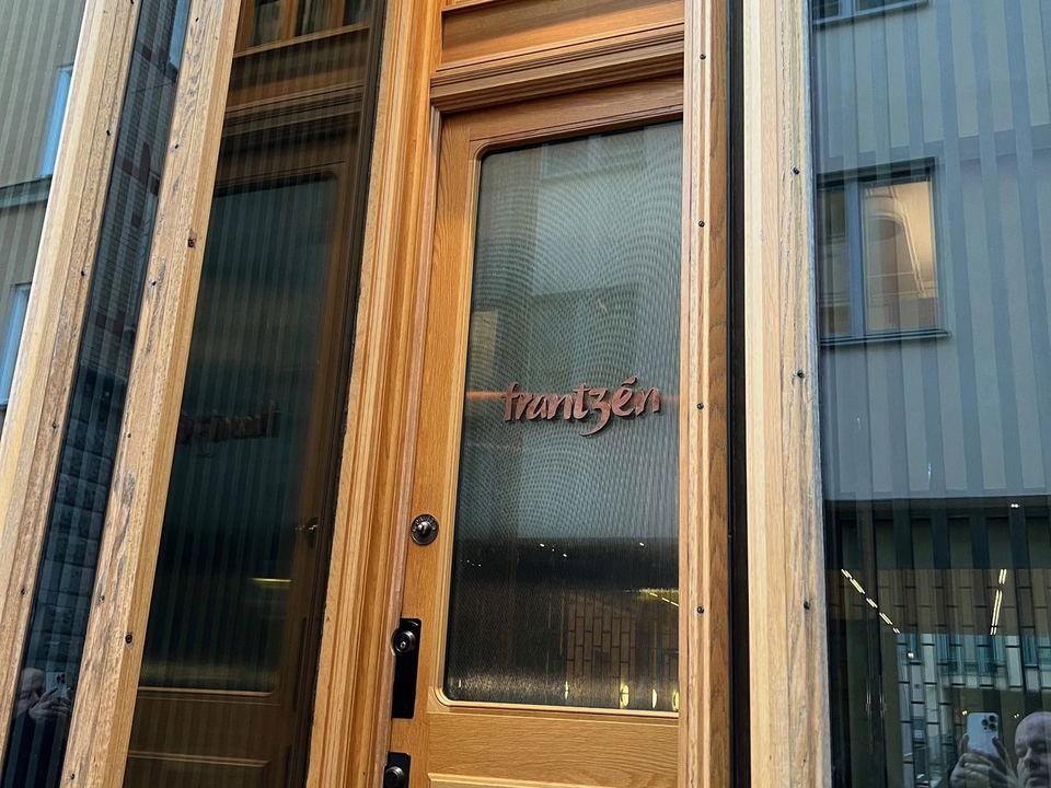 The wooden entrance door of Restaurant Frantzén, featuring a glass panel with the name "frantzén" and the number "26" above.