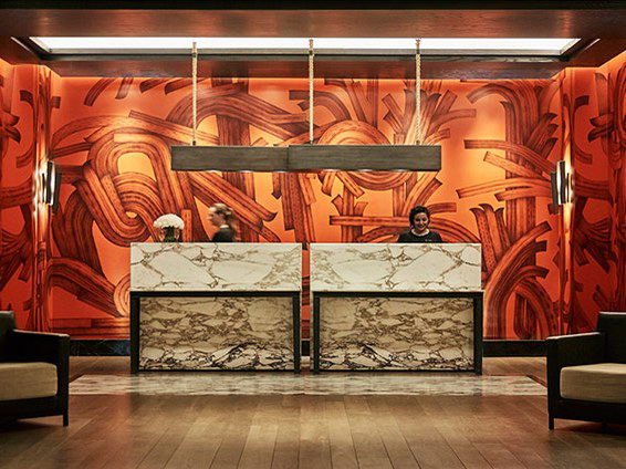 The reception desk of the Four Seasons Hotel Mexico City features two marble-topped counters against an orange abstract mural.