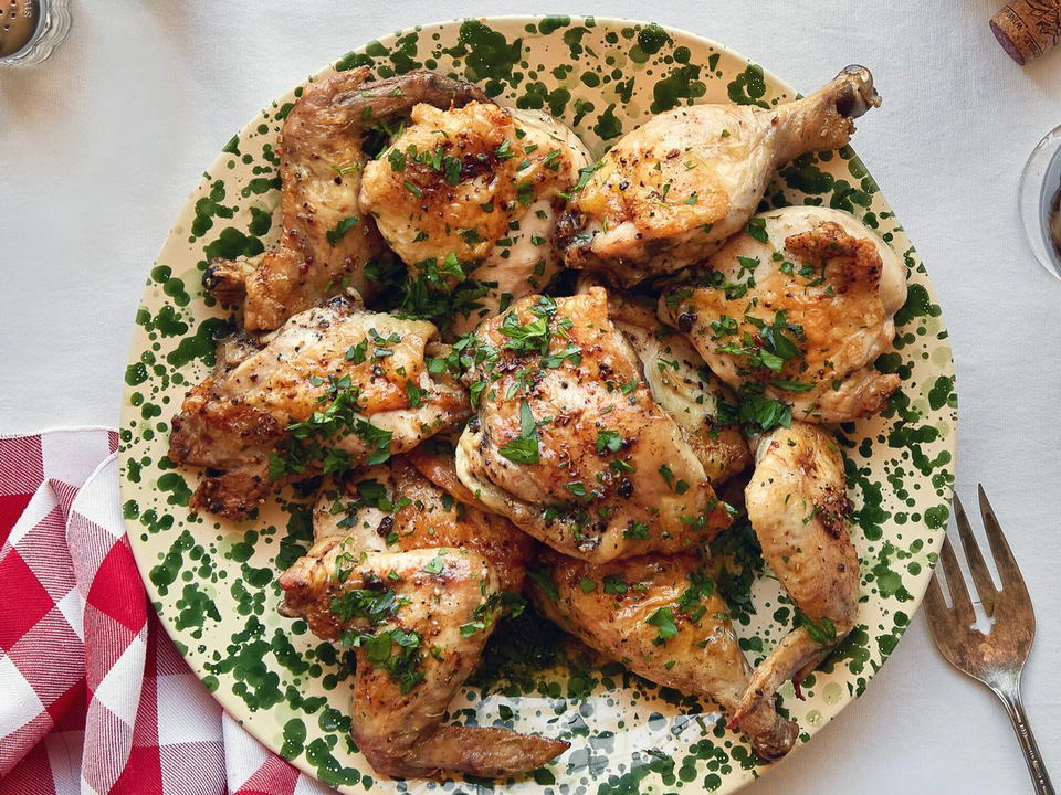 A platter of golden roasted chicken pieces garnished with fresh herbs, served alongside red wine glasses and a bottle.