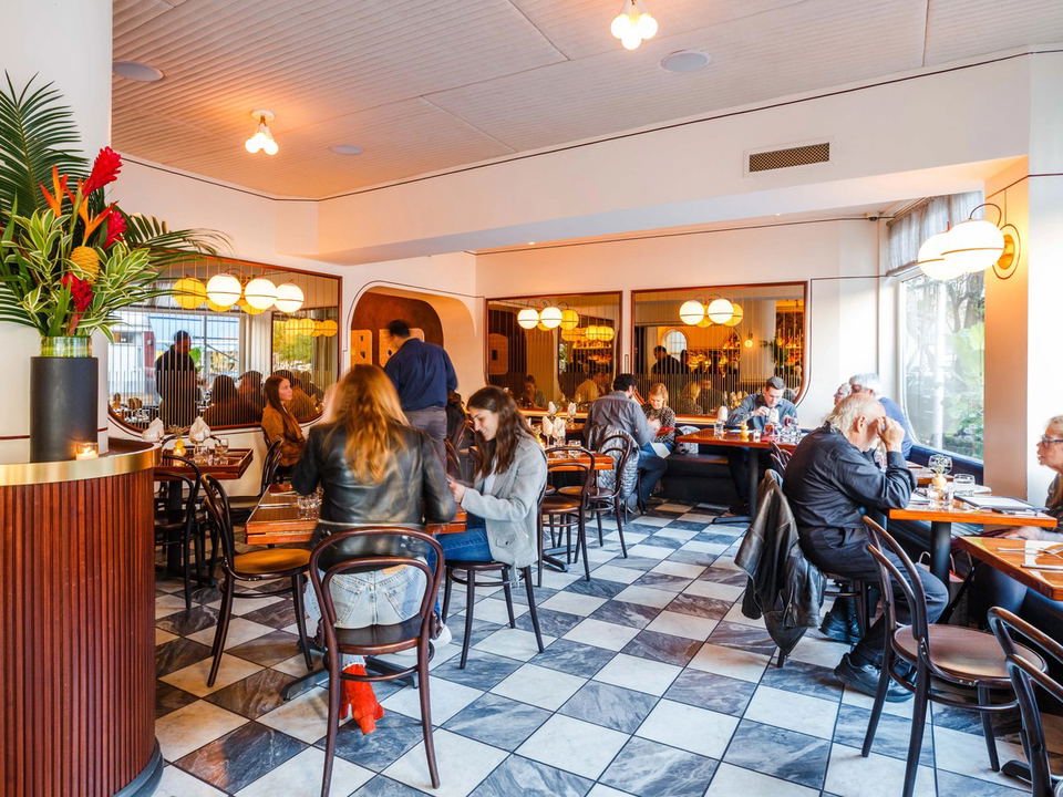 A bustling dining room at Don Angie's West Village location, featuring checkered marble floors, bentwood chairs, and globe pendant lights.