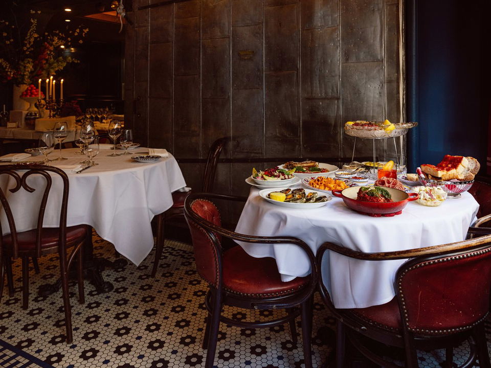 A dining room at Carbone's Greenwich Village features a white-tablecloth table laden with Italian-American dishes and red leather chairs.