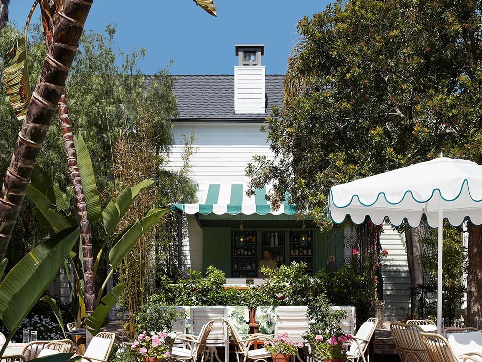 An outdoor pool area at San Vicente Bungalows with rattan lounge chairs, white-and-teal umbrellas, and a striped awning bar.