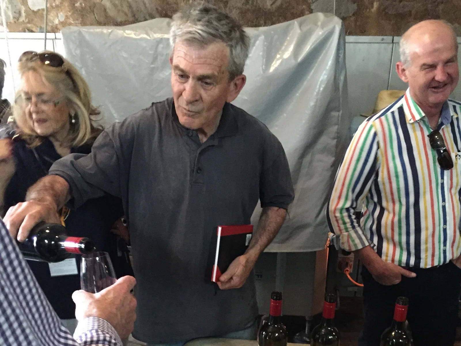 Tony Brady, a winemaker, pours red wine from a bottle into a glass for a person in a checkered shirt.