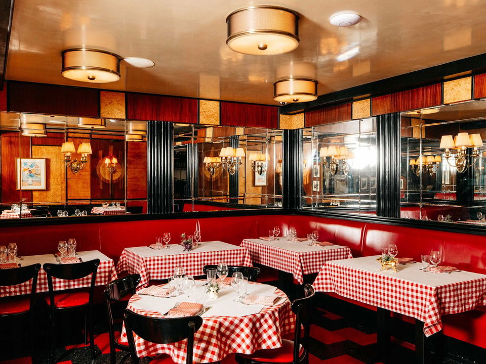 A classic French bistro dining room with red-and-white gingham tablecloths, red leather banquettes, mirrored walls, and warm lighting.