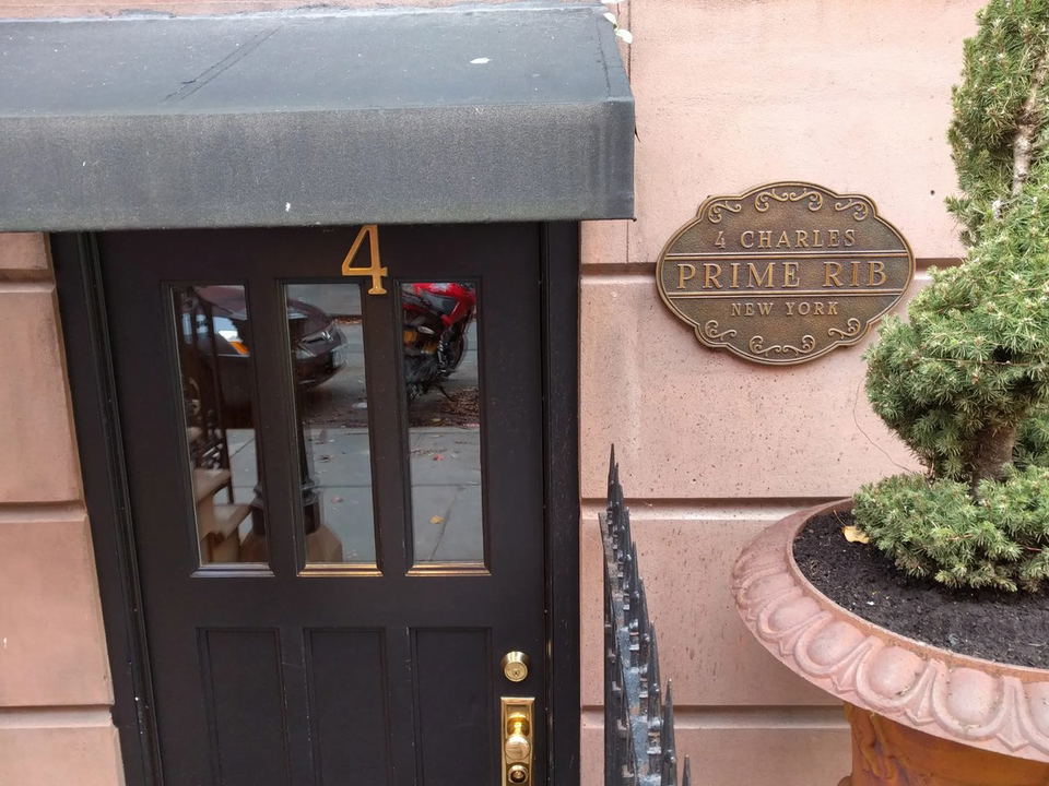 The black entrance door of 4 Charles Prime Rib, featuring the number '4' in gold, next to a bronze plaque reading '4 Charles Prime Rib New York'.