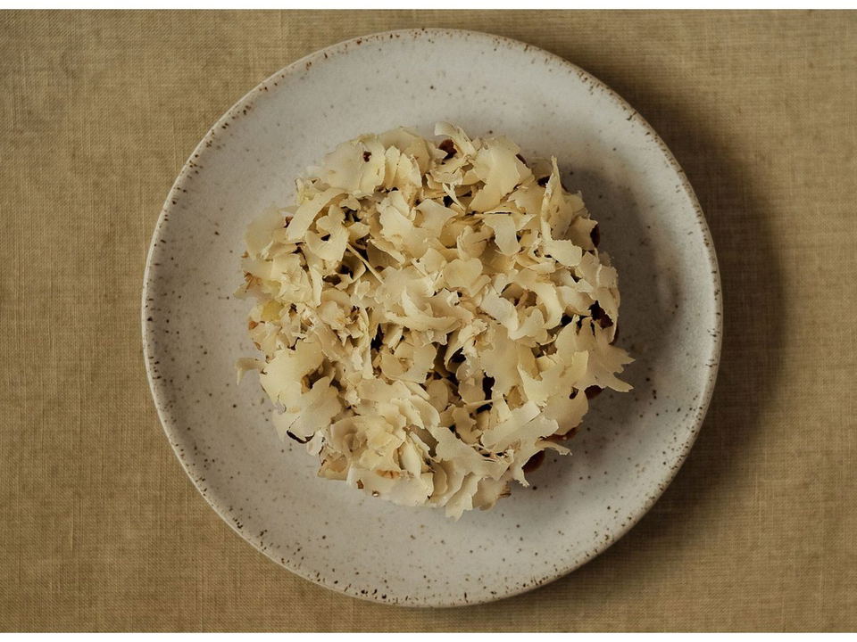 Overhead shot of toasted coconut flakes piled on a speckled ceramic plate, consistent with a Kadeau Copenhagen dish.