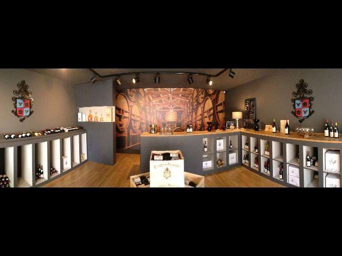 A panoramic interior view of La Cave Famille Perrin, showing a tasting counter, wine bottles on shelves, and a barrel mural.