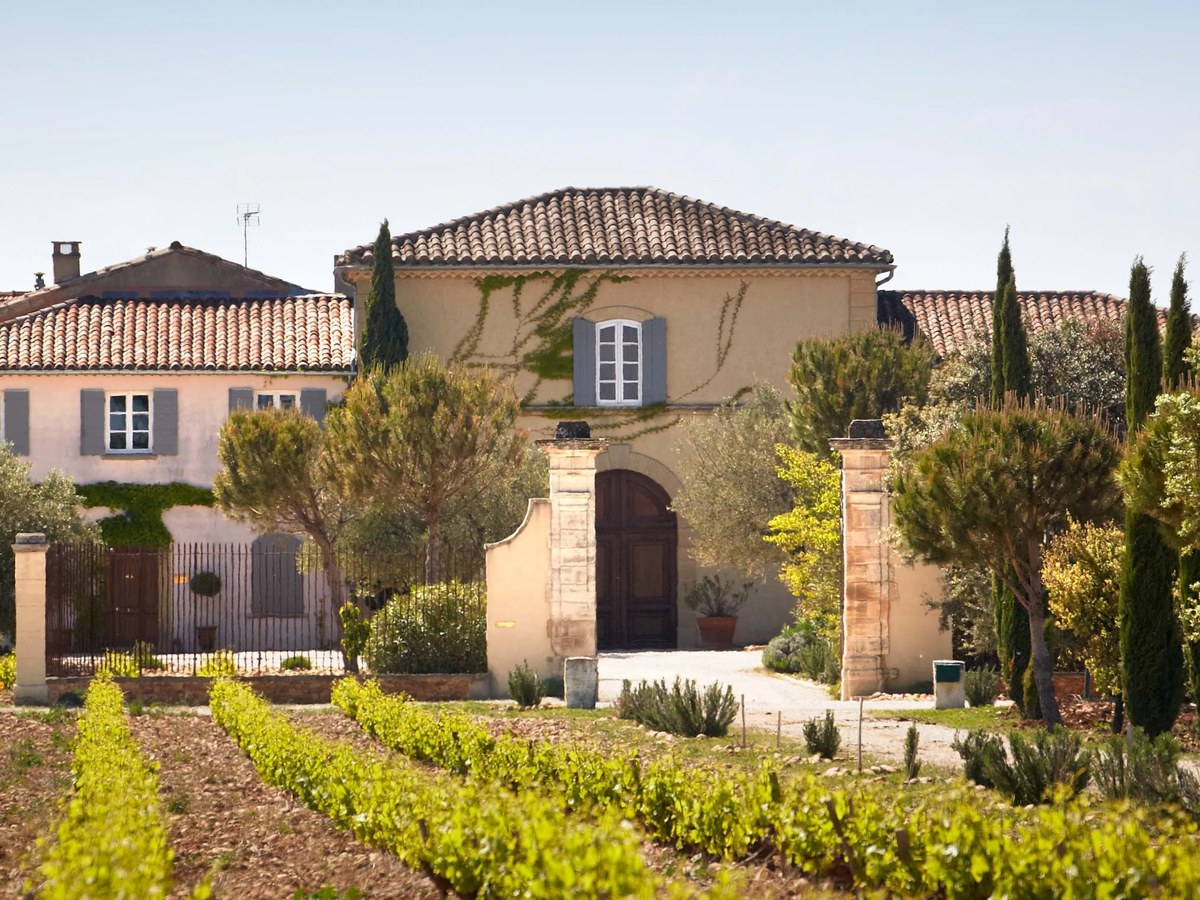 A panoramic view of Château de Beaucastel, featuring a traditional Provençal farmhouse with terracotta roofs, a stone archway, and rows of vibrant.
