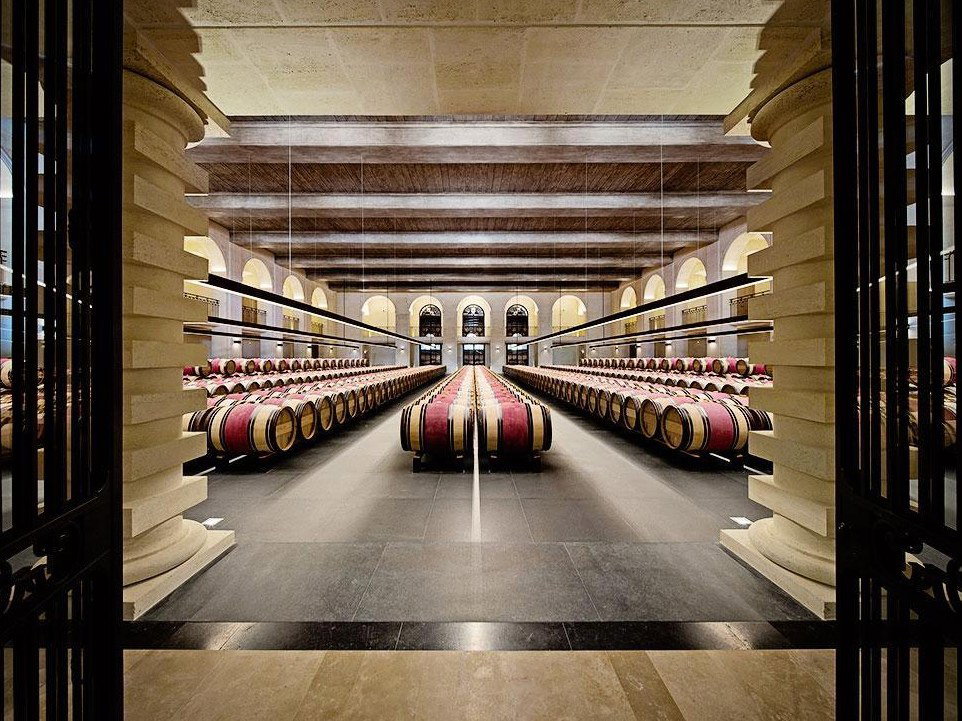 A grand, symmetrical barrel cellar at Château Montrose, with long rows of oak wine barrels stretching into the distance under arched ceilings.