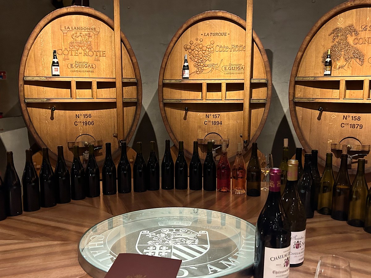 Large wooden wine barrels, adorned with labels and small bottles, stand behind a table lined with various wine bottles, creating an.