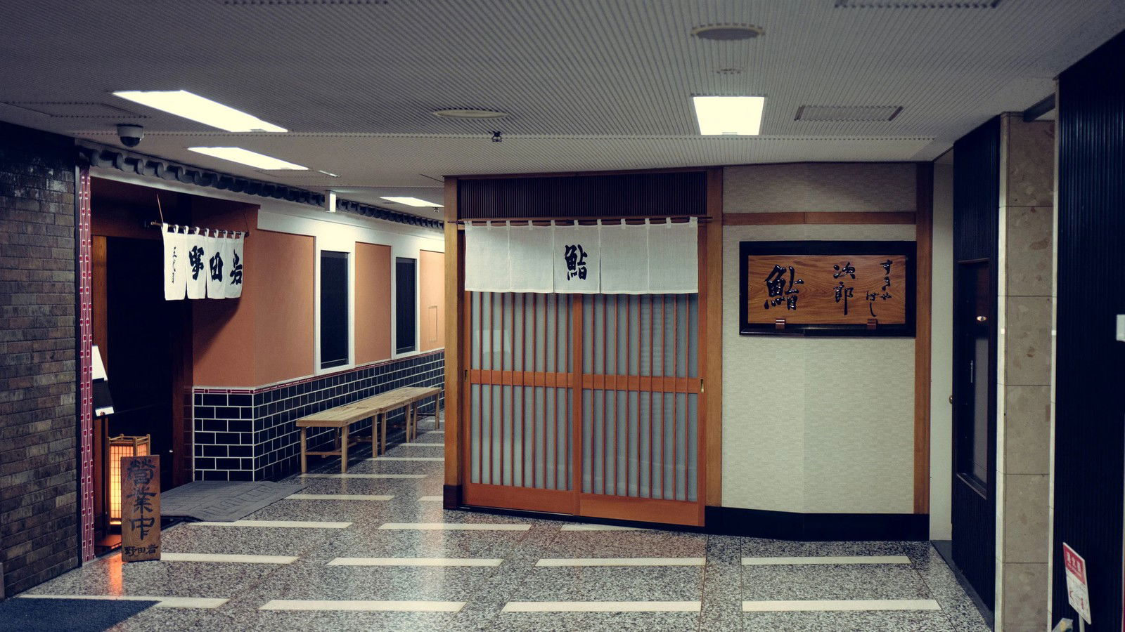 Sukiyabashi Jiro Honten in Ginza's entrance hallway, with traditional sliding doors, noren curtains, and terrazzo flooring.