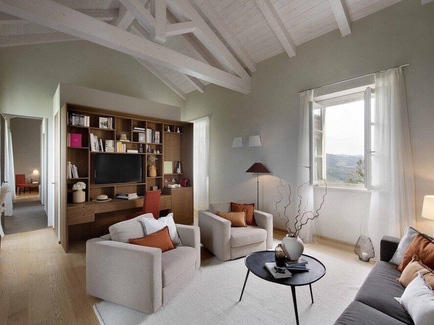 A bright, elegant living room at Relais San Maurizio with vaulted white-beamed ceilings, a large window, and light-colored furniture.