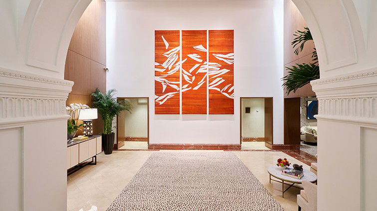 A grand hotel lobby interior with arched white columns, a large orange triptych artwork on the wall, marble flooring, and a runner rug.