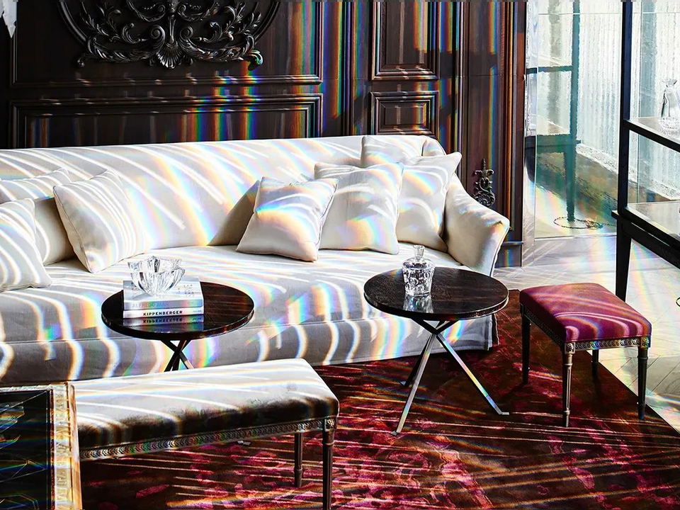 A luxurious lounge in the Baccarat Hotel's Petit Salon with a white sofa, dark wood paneling, and rainbow light refractions.