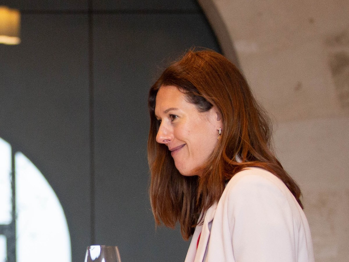 A woman smiles while holding a wine glass in a tasting room.