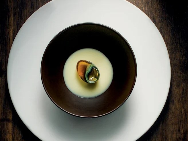 A fine-dining plated dish showing a quail egg in a dark bowl with pale broth, matching the caption 'Thousand-Year-Old Quail Egg, Potage, Ginger' from