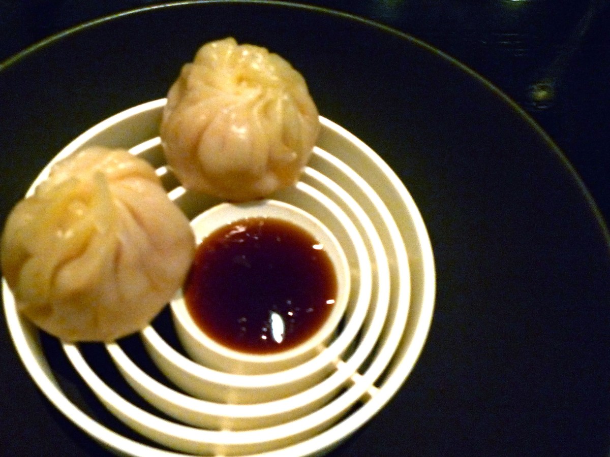Two steamed dumplings (likely xiao long bao) plated on a distinctive Korean ceramic vessel with concentric circular ridges, accompanied by a small dis