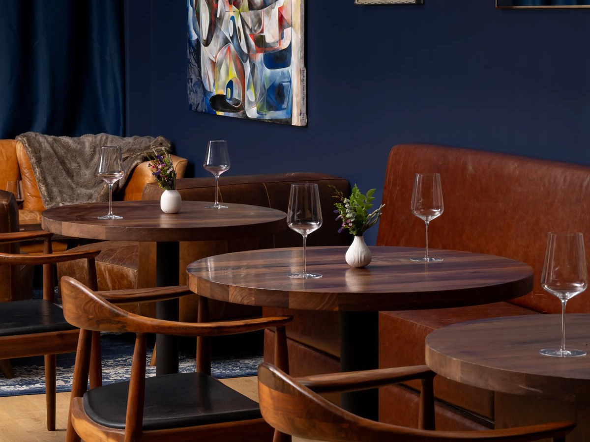 Saison: An inviting interior with round wooden tables, leather banquettes, and wine glasses.
