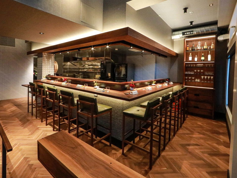 An empty omakase sushi counter at Friends Only in San Francisco, featuring green leather bar stools and a warm wood counter.