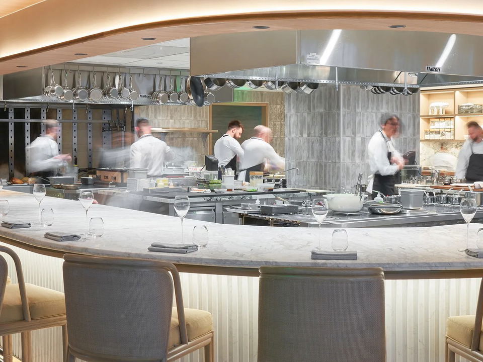 Maass restaurant: Chefs work in an open kitchen behind a curved marble bar with empty seats.
