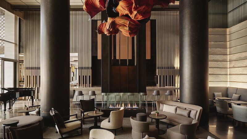 Aman Club New York: A luxurious lounge with a dramatic red sculpture, fireplace, and plush seating.