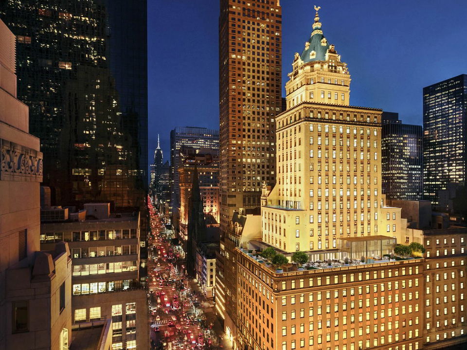 Aman Club New York's home, the Crown Building, glows over a bustling Fifth Avenue at dusk.