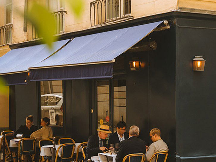 A classic Parisian café terrace with blue awnings and diners enjoying an outdoor meal in the 6th arrondissement.