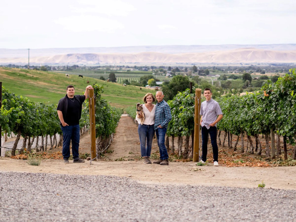 Vineyard with four people and a dog in front of grapevines.