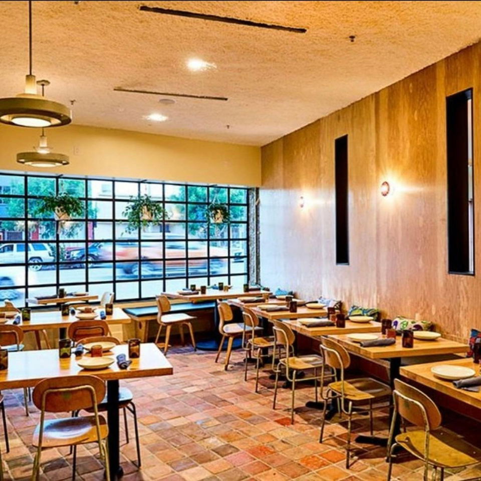 Alta Adams dining room with wood tables, chairs, tiled floor, and large street-facing windows.