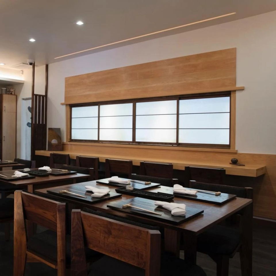 n/naka dining room with wooden tables, place settings, chairs, and shoji-style window panels.