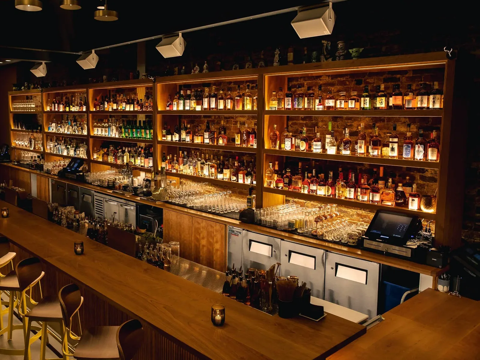 A long, well-lit bar with shelves of liquor bottles, glassware, and bar stools, creating an inviting atmosphere.