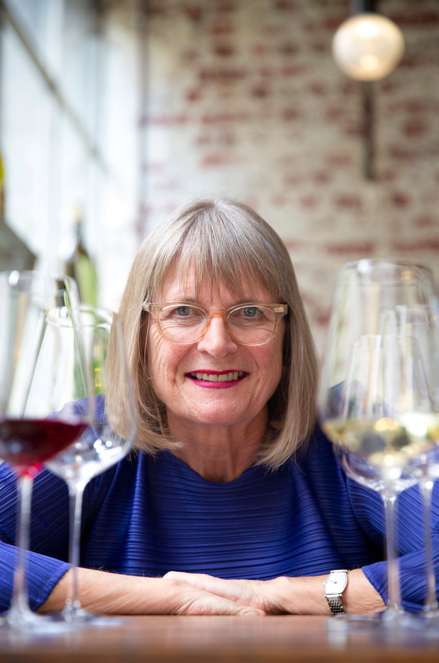 Professional portrait of a woman with shoulder-length gray hair and clear-framed glasses seated at a table with wine glasses, sourced from Decanter's