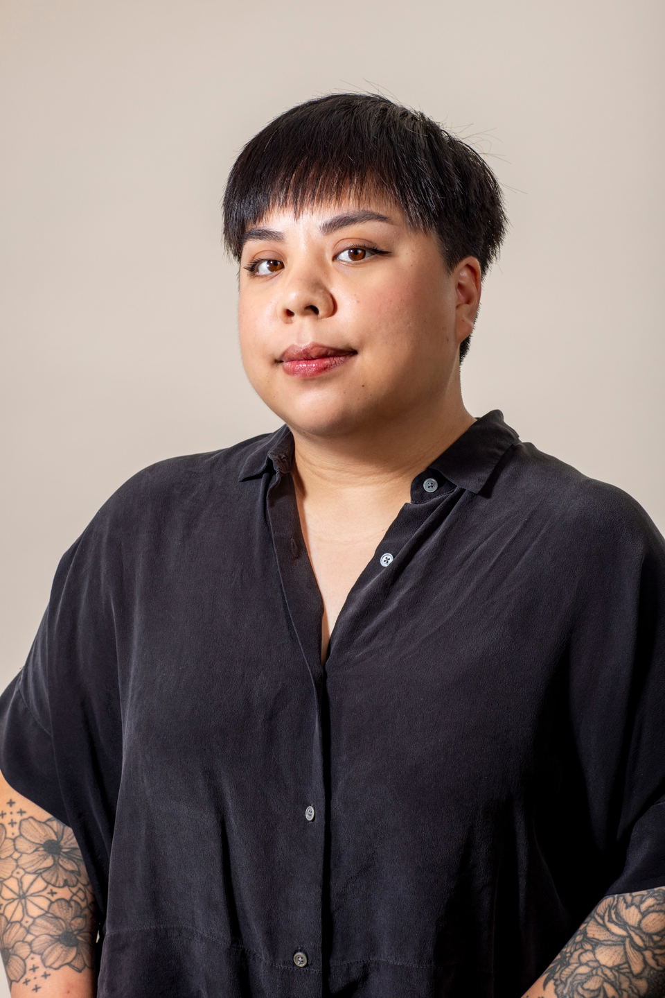 Professional editorial portrait of a person in a black button-up shirt against a neutral background