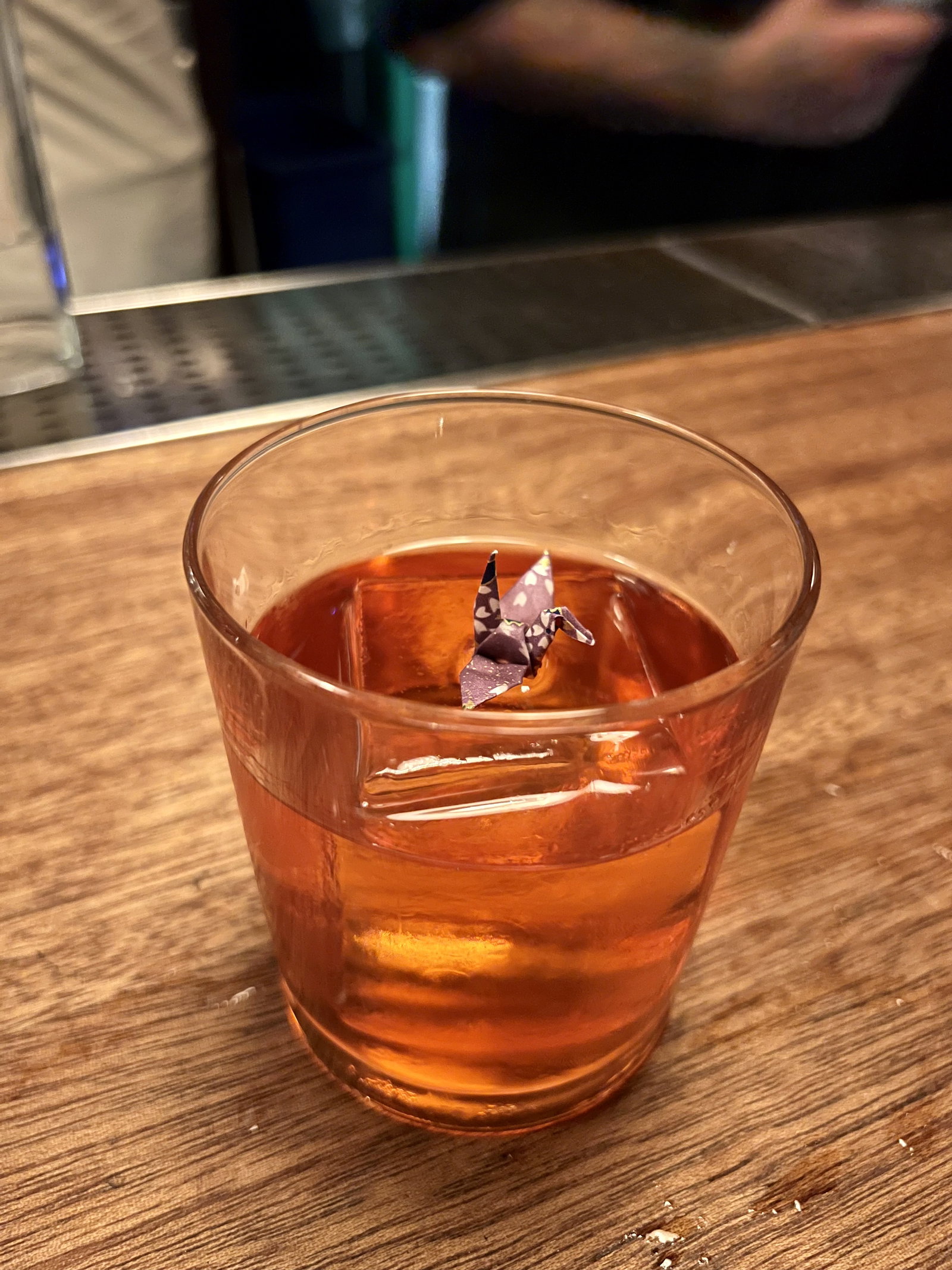 a cocktail on a bar with a paper crane