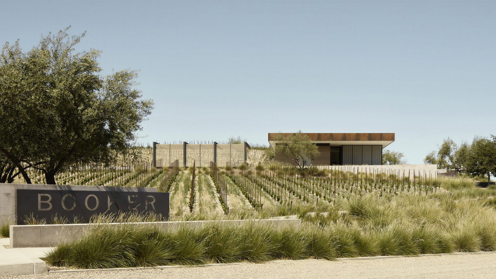 Modern vineyard with rows of grapevines and a sleek building amidst trees. "BOOKER" sign in the foreground. Calm and serene atmosphere.
