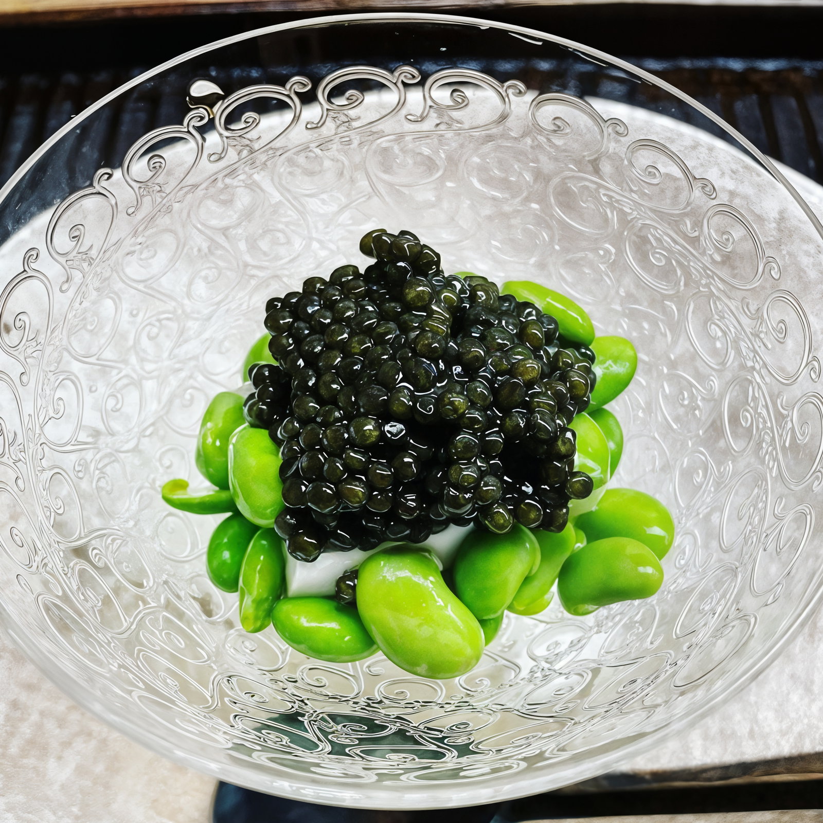 Caviar atop bright green edamame in a decorative glass bowl. Elegant design and textured pattern on bowl enhance a refined culinary presentation.