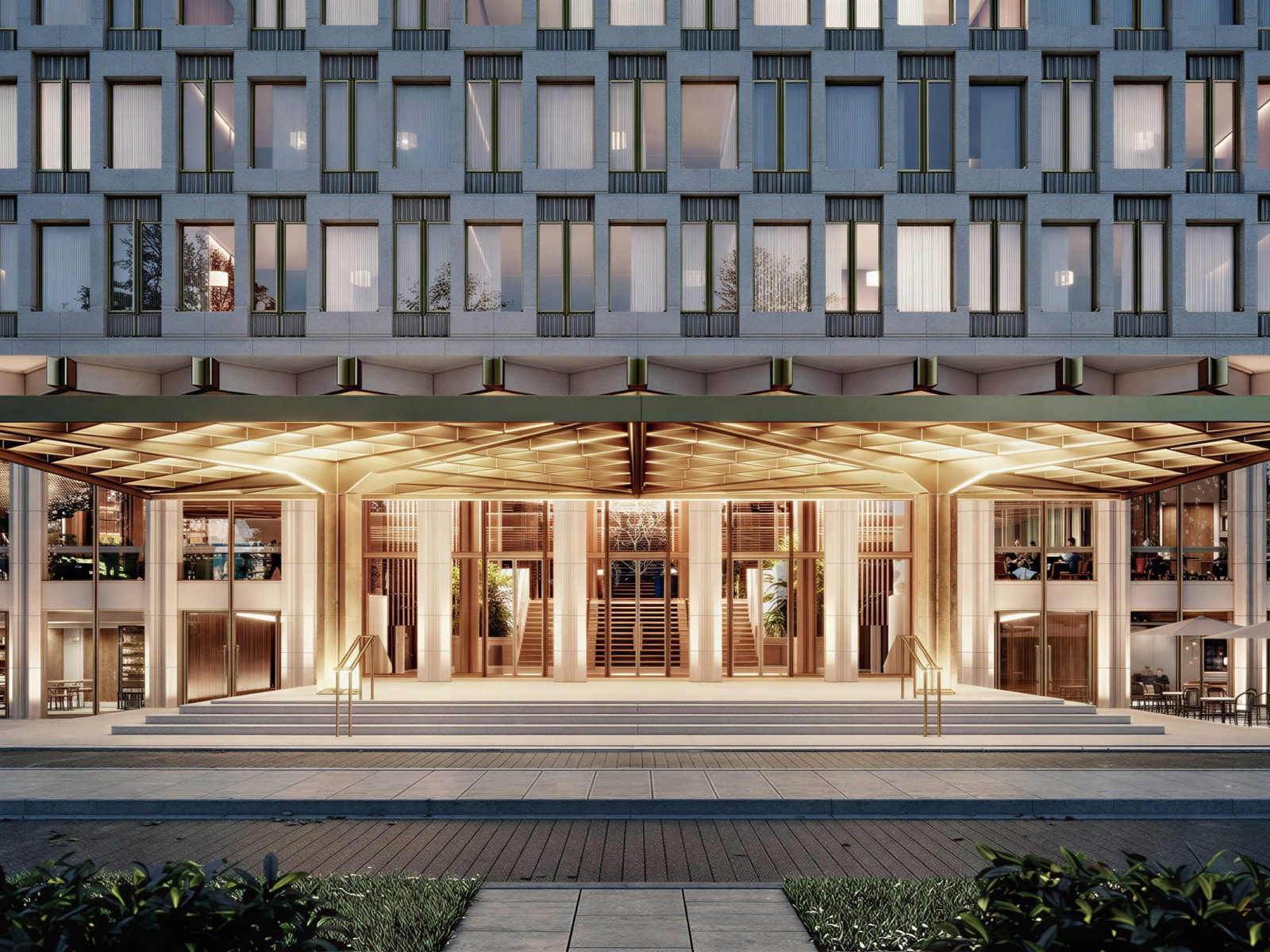 Elegant entrance to The Chancery Rosewood London with golden lighting, large glass doors, and stone steps. Rows of windows above. Indoor seating and umbrellas visible.
