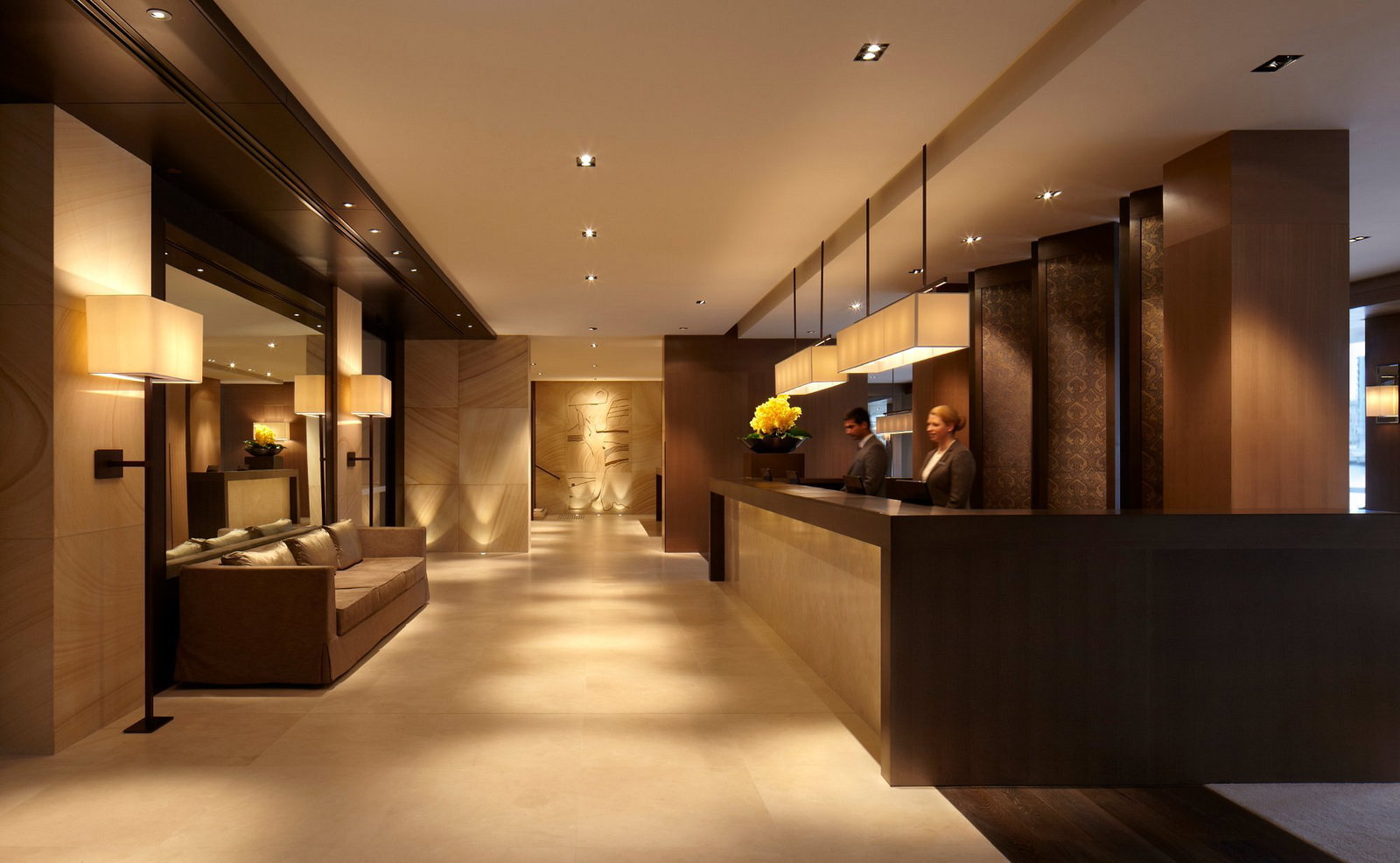 Park Hyatt Sydney Reception with two staff at a wooden reception desk. Warm lighting, beige tones, and modern decor create a welcoming atmosphere.