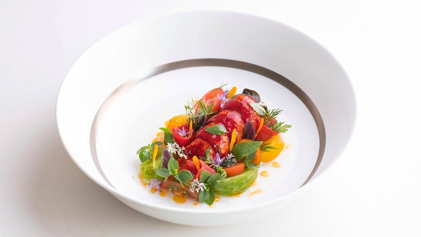 Elegant dish with vibrant red lobster, colorful vegetables, herbs, and edible flowers, artfully arranged on a white plate.