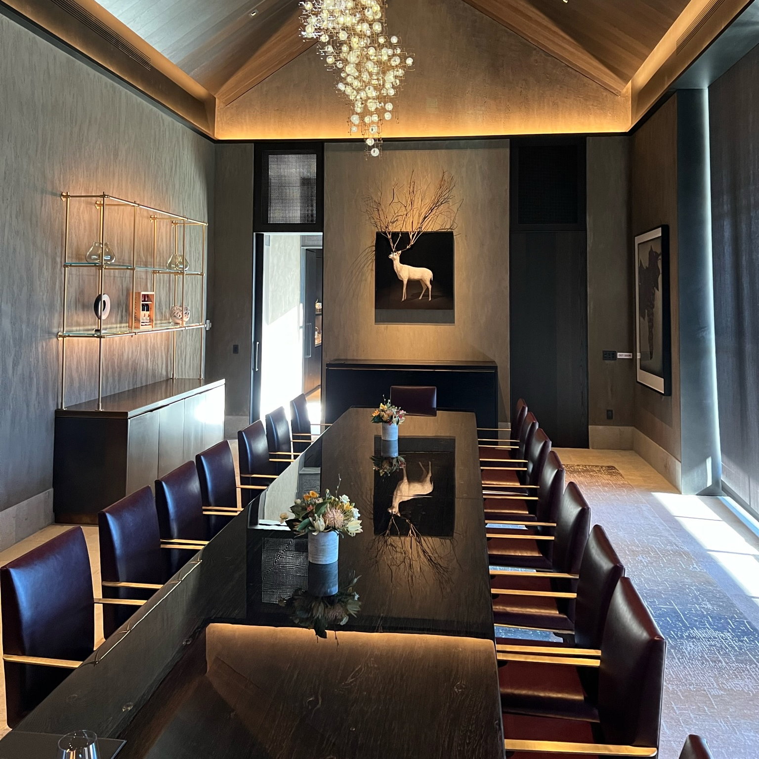 Elegant dining room with a long black table set with flowers. Art piece of a deer on the wall. Modern chandelier hanging above.
