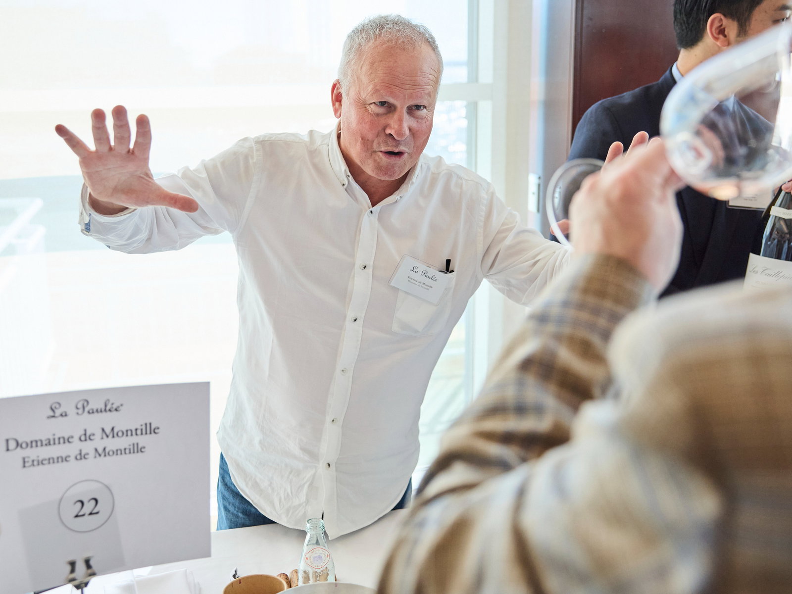 Winemaker Etienne de Montille explains his wines at The Grand Tasting of La Paulée NYC 2025. A person in plaid holds a wine glass. Sign reads "Domaine de Montille."