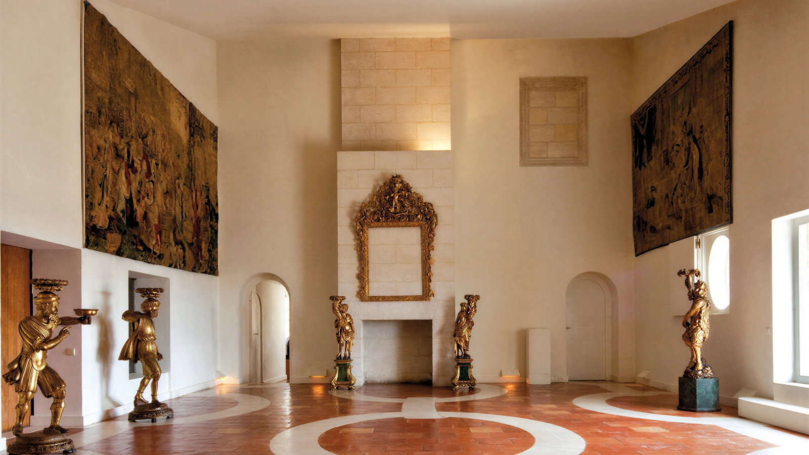 Elegant room with ornate gold statues and intricate tapestries on beige walls. Brick floor with white patterns, creating a serene ambiance.
