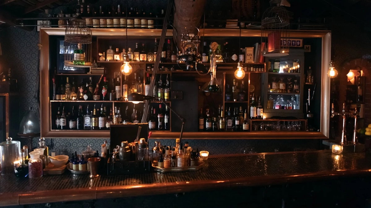 Dimly lit bar with bottles on shelves, glowing pendant lights, and a rustic, cozy atmosphere. Dark wood and vintage decor add charm.