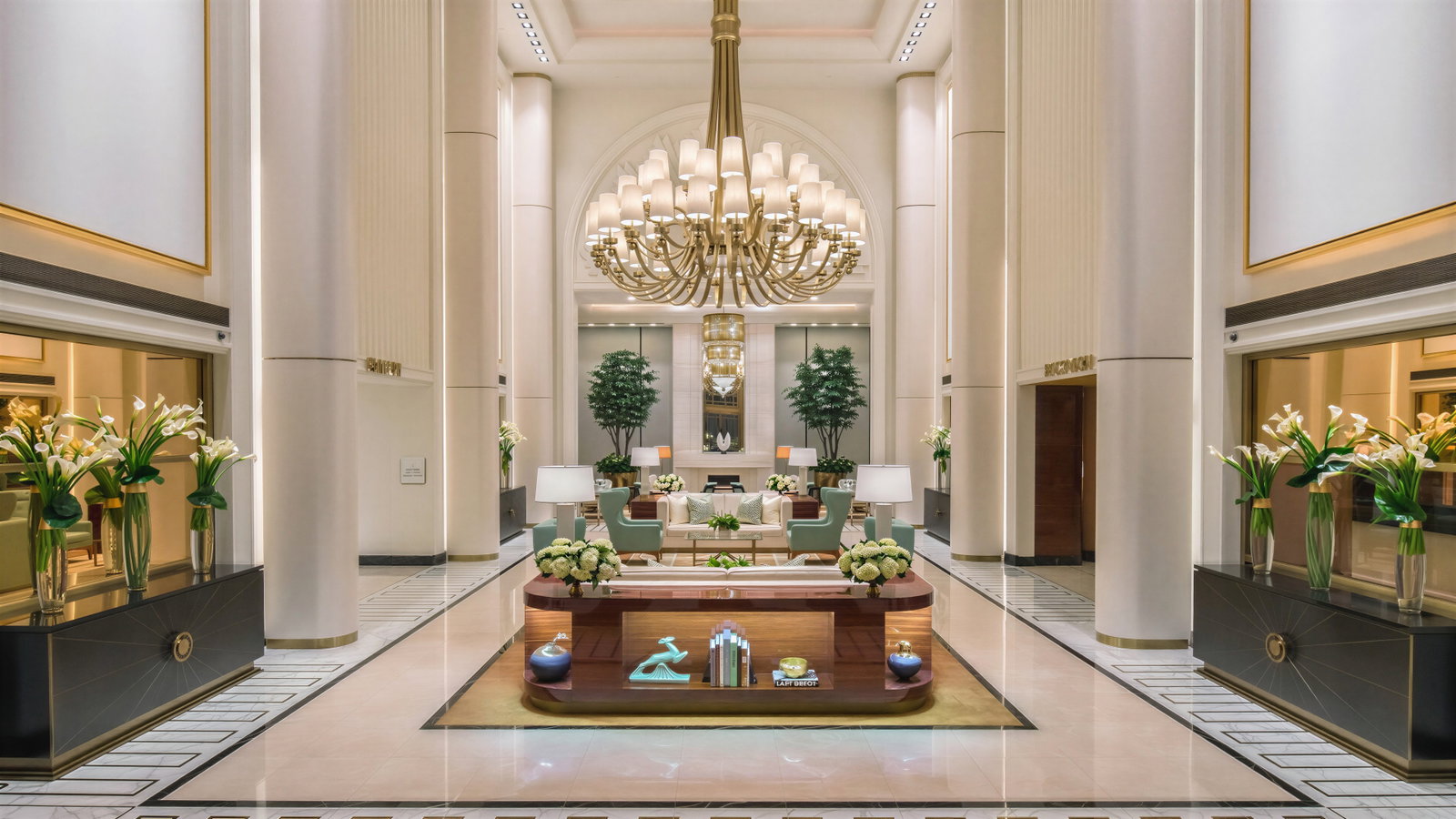 Elegant hotel lobby with a grand chandelier, marble floors, and floral arrangements. Soft lighting and neutral colors create a serene atmosphere. (AI-generated, newly added)