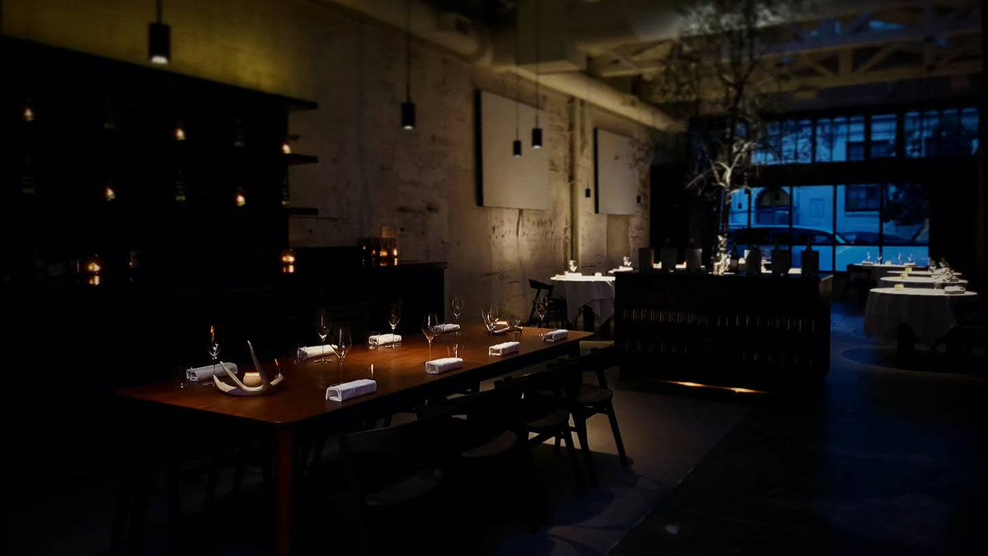 Dimly lit, elegant restaurant interior with set tables, candles, and wine glasses. Warm tones and a peaceful, sophisticated ambiance.