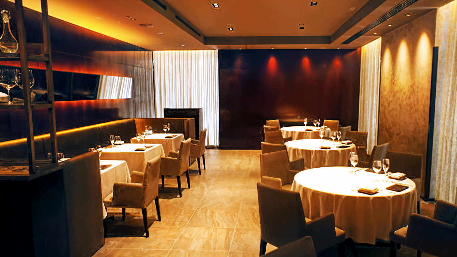 Elegant restaurant interior with round tables and beige chairs. Warm lighting and modern decor create a cozy, upscale atmosphere.