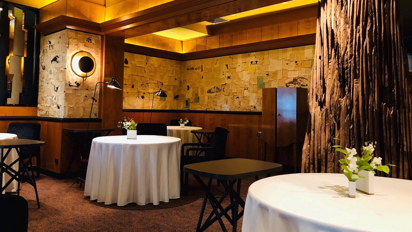 Cozy restaurant with white tablecloths, floral centerpieces, and artistic wall decor. Warm lighting creates an inviting atmosphere.